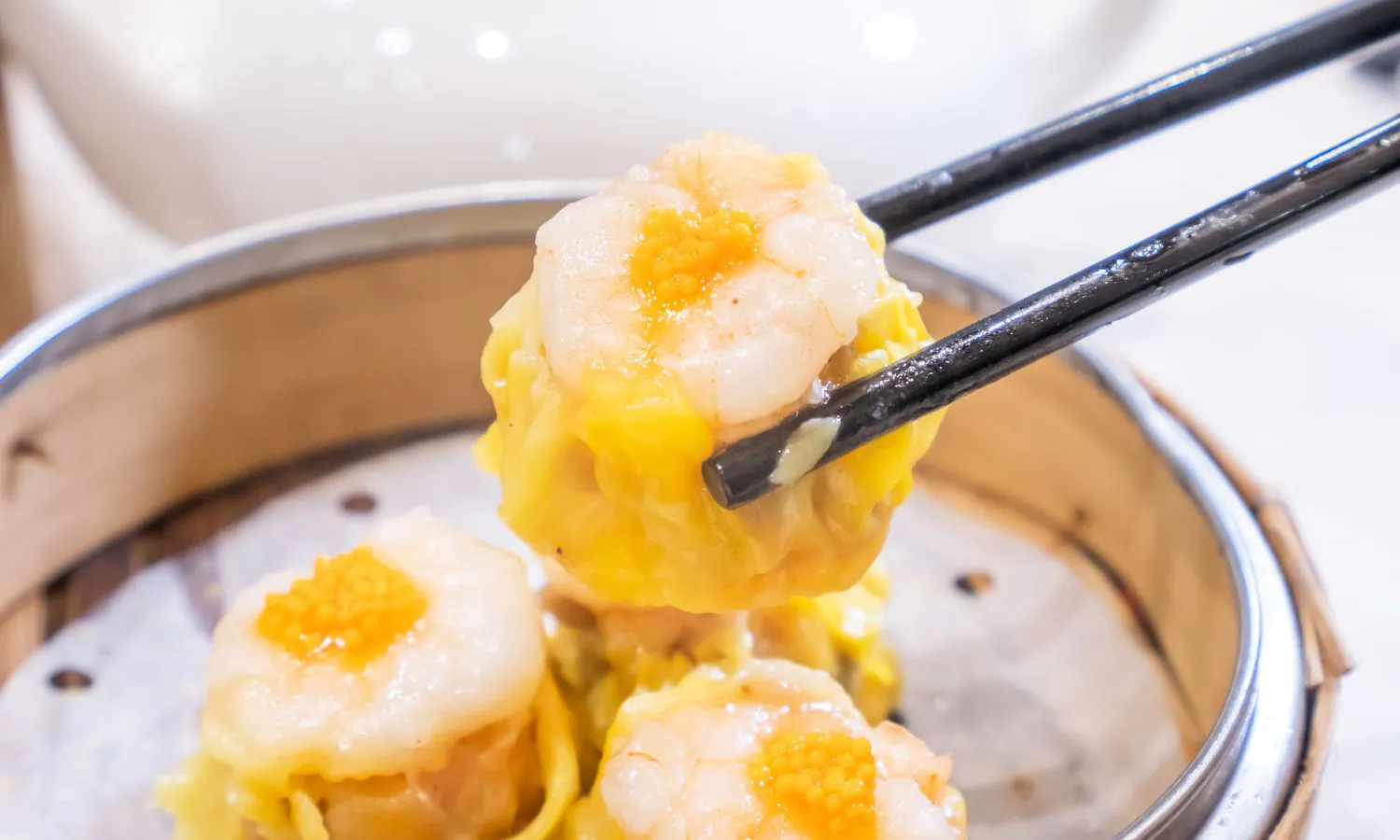 Shrimp siu mai topped with roe held by black chopsticks