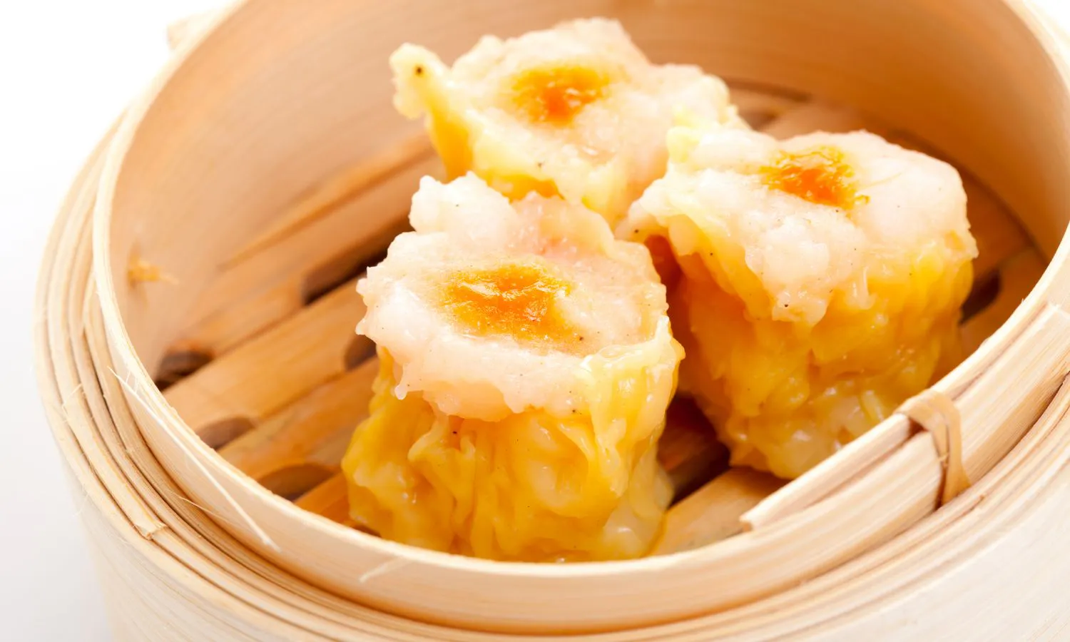 Three pieces of roe-topped siu mai inside bamboo steamer